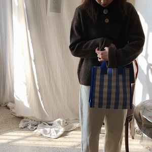 Detail of blue and white checkered tote bag held by a model in a minimalist home setting