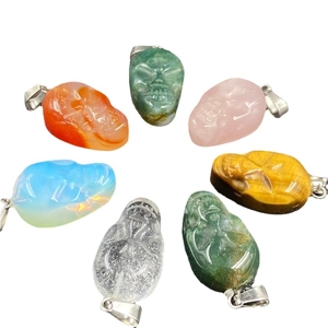 Variety of carved crystal and gemstone skull pendants with silver loops on white background