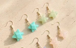 Detail of multi-colored Merkaba star crystal earrings on a textured black display tray
