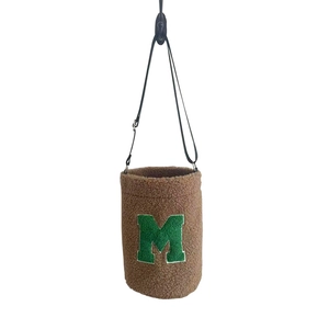 Brown fuzzy faux shearling bucket bag with green letter M patch and black shoulder strap