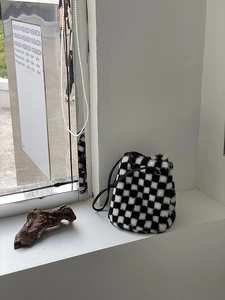 Détail du sac seau en peluche à damier avec cordon sur un rebord de fenêtre blanc