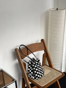Sac seau en peluche à damier avec lanières en cuir sur une chaise en rotin rétro