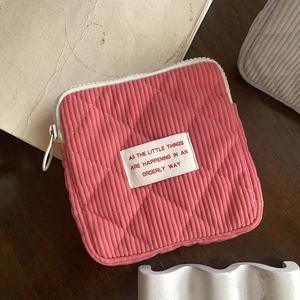 Pink corduroy quilted cosmetic bag with woven label detail on a wooden desk setup
