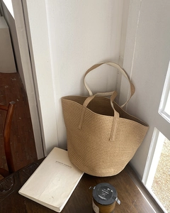 Detail of hand-woven straw tote bag with dual handles on a rustic wooden table