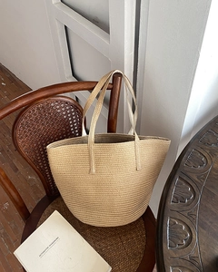 Close-up of woven straw handbag texture and handles on a wooden chair backdrop