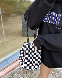 Détail du sac seau en peluche à damier avec bandoulière en cuir porté par un mannequin