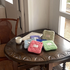 Close-up of quilted corduroy mini makeup bags in various pastel colors on a wooden table