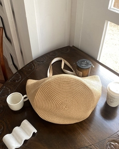 Detail of a large beige straw woven bucket bag placed on a rustic dark wooden tabletop