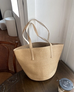 Detailed texture of a beige woven straw bucket bag on a vintage wooden table surface