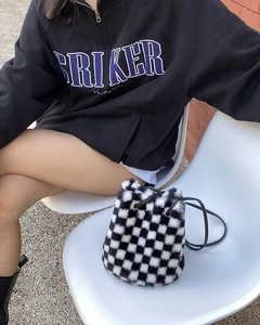 Détail du sac seau en peluche à damier avec cordon de serrage posé sur une chaise blanche