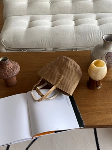 Detail of hand-woven straw tote bag with textured horizontal weave on a wooden table