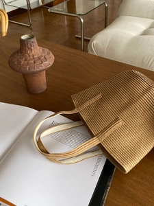 Detailed top view of a brown woven straw tote bag on a wooden table with art magazines