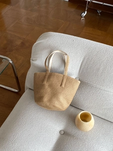 Close-up of natural straw hand-woven tote bag with dual handles on white fabric