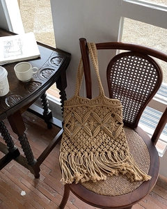 Detailed macro view of beige handmade macrame bag with tassels on a rattan chair