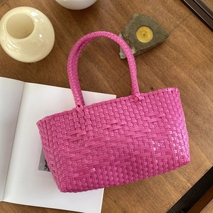 Handmade woven basket bag in vibrant rose pink on a wooden surface with lifestyle decor