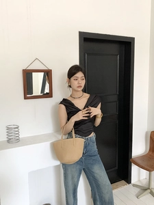 Lifestyle shot of large capacity woven straw bucket bag with blue jeans and black top