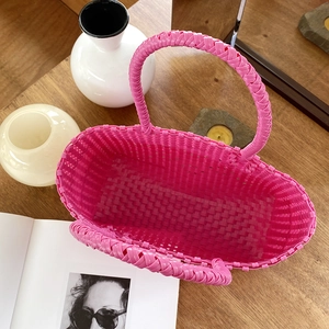 Bright pink handmade woven basket bag with round handles on a wooden table setup