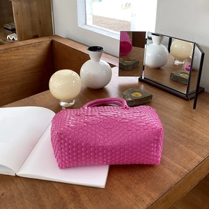 Detail of rose pink hand-woven basket bag with textured weave on a dark wood table
