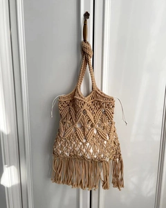 Detail of handmade macrame straw bag featuring geometric weave and long fringe tassels