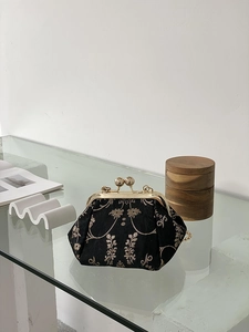 Detail of vintage black kiss-lock bag with gold floral embroidery on glass table