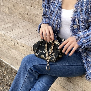Close-up of black fabric vintage clutch with golden floral embroidery and metal chain