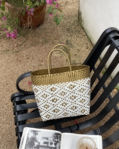Detailed close-up of woven straw beach tote bag on iron bench with summer garden background