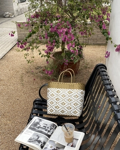 Detail of a gold and white woven tote bag on a bench with bougainvillea flowers