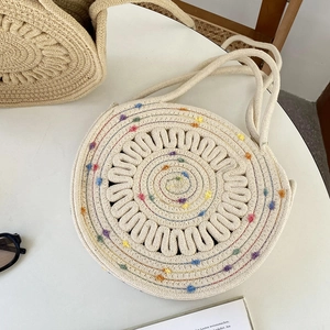 Détail d'un sac rond en paille tissée avec broderies colorées et anses en coton