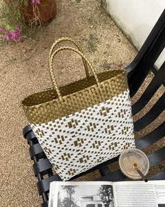 Close-up of gold and white woven tote bag with round handles on a park bench