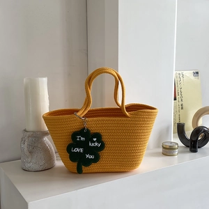 Detail of yellow woven basket bag with a green lucky clover charm and embroidery