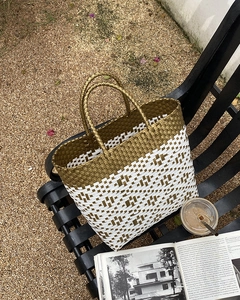 Detail of gold and white checkered woven tote bag with round handles on a bench