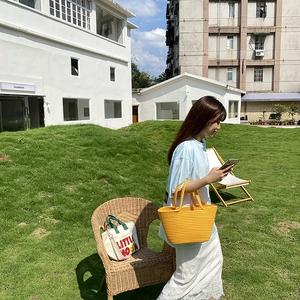 Detailed outdoor shot of a vibrant yellow hand-woven straw tote with rope handles