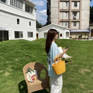 Detail of yellow woven handmade tote bag on grass with model in casual outfit