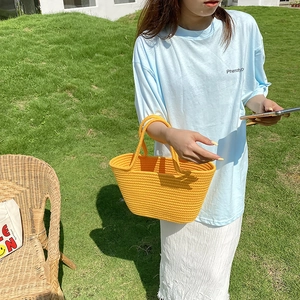 Detail of a bright yellow woven cotton rope handbag held by a model in a natural setting