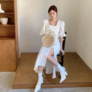 Sac à main rond en paille avec robe en lin blanc dans un décor intérieur minimaliste