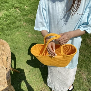 Close-up of bright yellow hand-woven straw bag with thick crochet texture on green grass