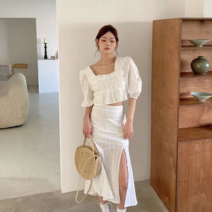 Détail d'un crop top blanc à manches bouffantes assorti à un sac à main en paille tressée