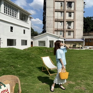 Outdoor shot of light blue cotton t-shirt paired with a woven straw tote bag and white skirt