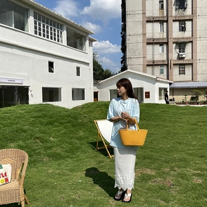 Detail of bright yellow woven tote bag carried by model against white building background