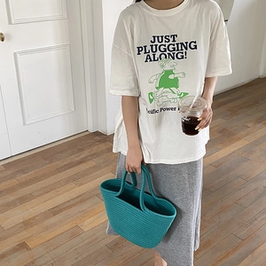Lifestyle view of a blue woven straw handbag paired with a casual white graphic T-shirt