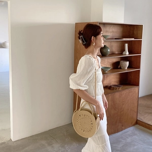 Détail d'un sac rond en paille tissée avec une robe blanche à manches bouffantes
