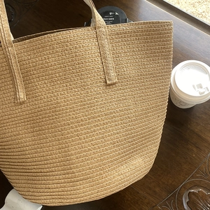 Handwoven straw tote bag with dual handles on a wooden table with a coffee cup