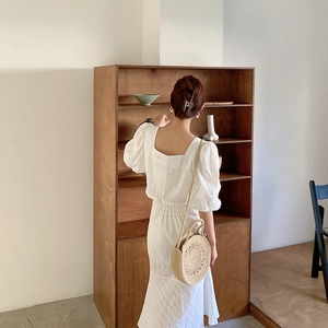 Détail du sac bandoulière rond en paille porté avec une robe longue blanche