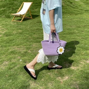 Detail of hand-woven purple straw bag with a white daisy charm on sunny grass