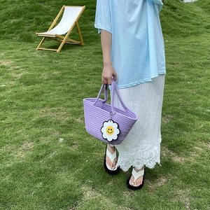 Detail of purple woven cotton rope bag with daisy smiley pendant against grass background