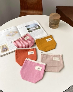 Flat lay of colorful canvas zipper pouches with woven labels on a minimal white table