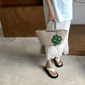 Handmade woven straw tote bag with lucky clover charm and beige texture for summer beach