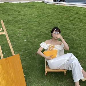 Outdoor summer scene with a bright yellow hand-woven handbag on a wooden chair