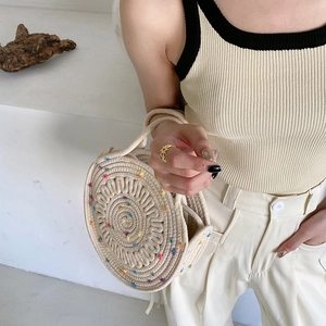 Gros plan d'un sac rond en paille tressée avec pompons colorés et poignées circulaires