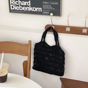Detail of black hand-woven cotton rope mesh tote bag hanging in a minimalist interior